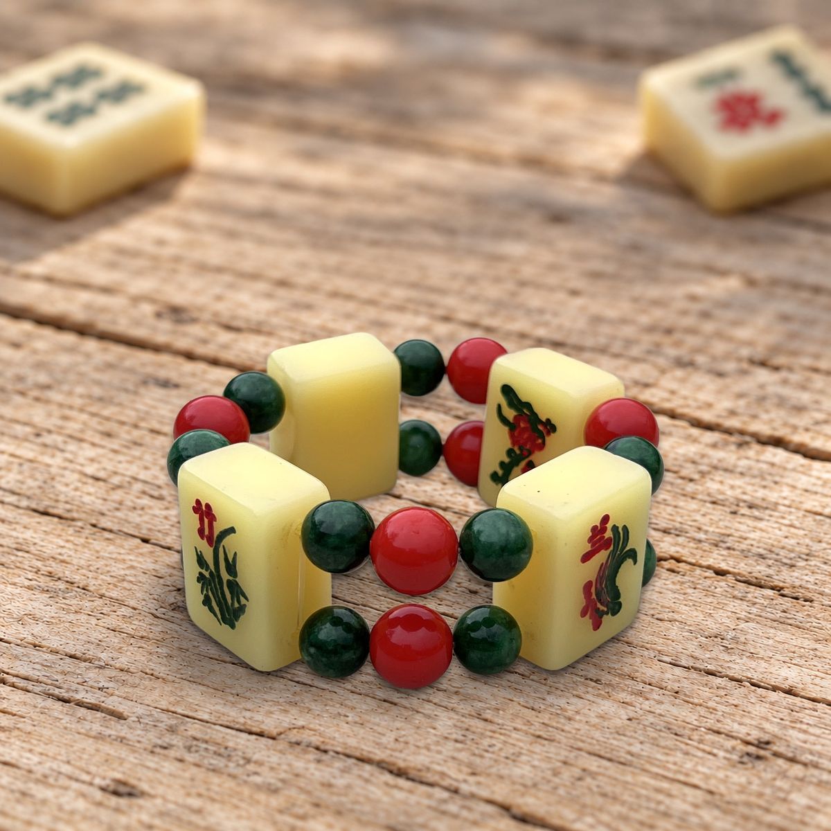 Bracelet Les Fleurs : tuiles de mahjong à motifs de fleurs, perles rouges et vertes, posé sur un vieux bois