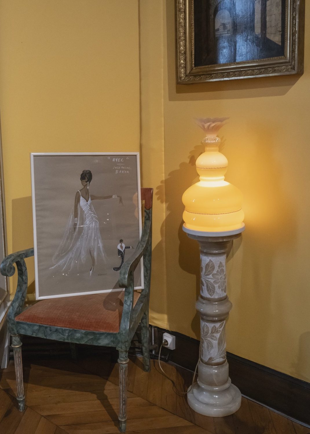 Lampe opaline de la série Lumineuse Joséphine posée sur une colonne, près d'un dessin de Joséphine Baker en robe du soir